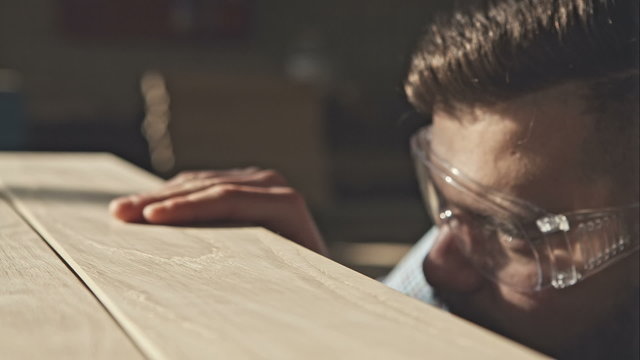 A young bearded carpenter checks the quality of the boards in the sun. RAW video record.