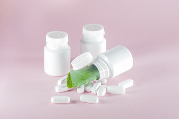 Sliced green leaves of aloe with homeopathic red capsules on a light pink background