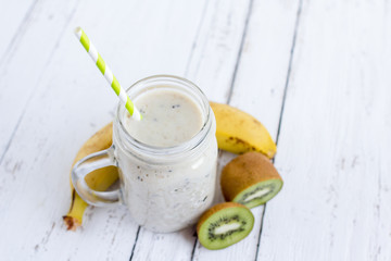Smoothie with banana, kiwi and milk on white wooden background,