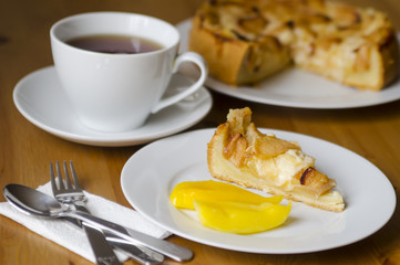 Table served to tea drinking. White cup of tea, paper napkin, cutlery and apple homemade pei  on the wooden table.
