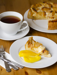 Table served to tea drinking. White cup of tea, paper napkin, cutlery and apple homemade pei  on the wooden table.