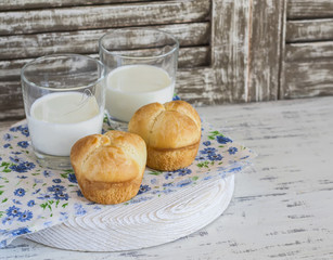 Buns and glasses of milk on a light rustic wood background.