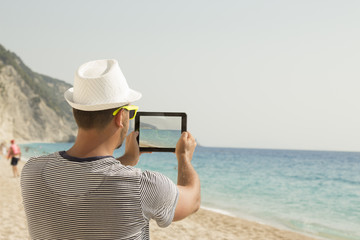Guy taking a photo of a beach with his digital tablet device