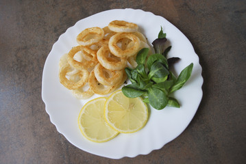 Cooked squid rings with green salad and lemon on white dish.