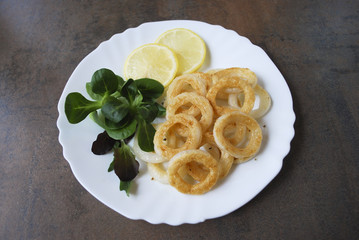 Cooked squid rings with green salad and lemon on white dish.