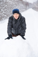 Fototapeta na wymiar Boy rolls a big snowball to build a snowman in winter day