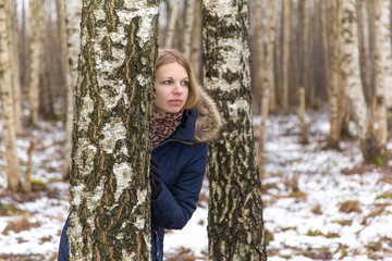 Nice, beautiful young lady hiding behind birch tree in the park