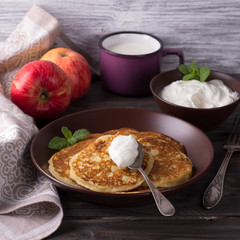Cottage cheese pancake with apples in ceramic bowl with sour cream and a glass of milk on a dark wooden table