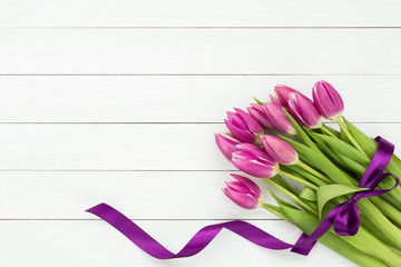 Bouquet of pink tulips decorated with purple ribbon on white wooden background. Top view, copy space