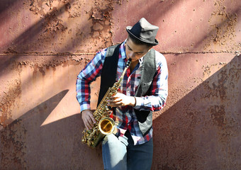 Young man playing on saxophone outside near the old wall