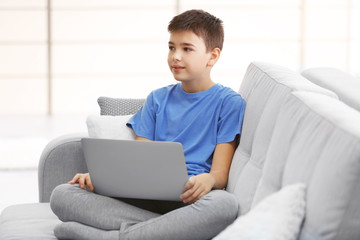 Little boy using laptop on a sofa at home