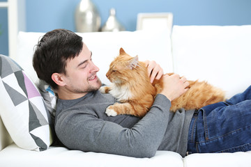 Young man with fluffy cat lying on a sofa