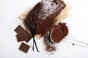 Chocolate cake with cocoa powder, vanilla pods on white table