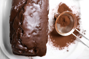 Chocolate cake with icing and cocoa powder on white table