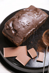 Chocolate cake with icing and cocoa powder on baking dish over white table