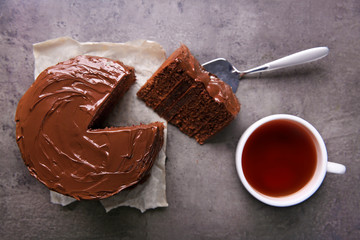 Chocolate cake with a cut piece and blade and cup of tea on gray background, closeup