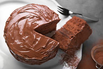 Chocolate cake on plate with a cut piece and fork and cocoa on gray background, closeup