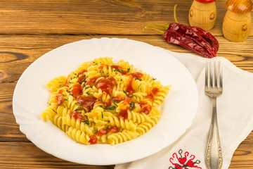 Italian pasta fusilli with tomato sauce in plate, napkin and fork on wooden table