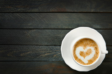 Cup of hot cappuccino with cream heart on a black wooden table