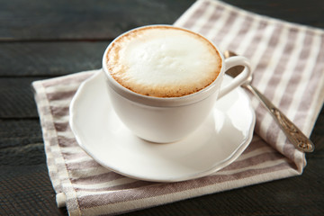 Cup of hot cappuccino with froth and spoon on a black wooden table