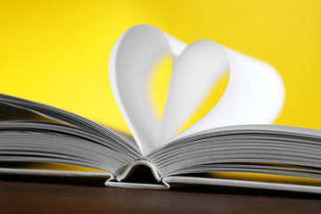 Heart from book pages on yellow blurred background