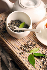 Granulated tea with green leaves in tea-set on wicker tray closeup