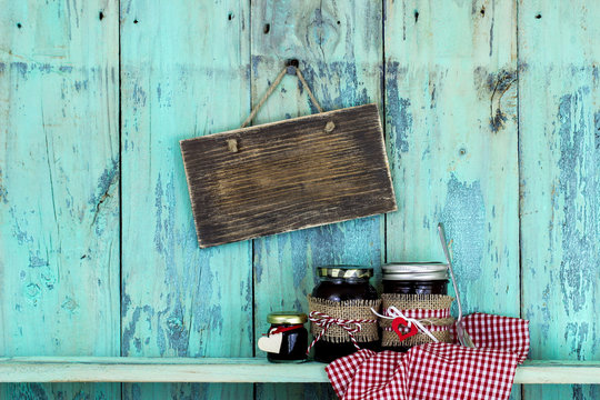 Blank rustic sign hanging on rustic teal blue background over jars of fruit jelly 