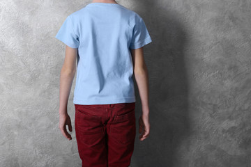 Clothes advertising. Boy in T-shirt and red trousers against grey textured wall background, back view