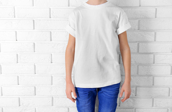 Clothes advertising. Boy in T-shirt and jeans on white brick wall background, close up