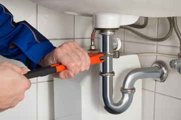 Male Plumber Repairing Sink In Bathroom