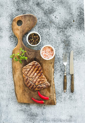 Grilled ribeye beef steak with herbs and spices on walnut cutting board over grunge grey background