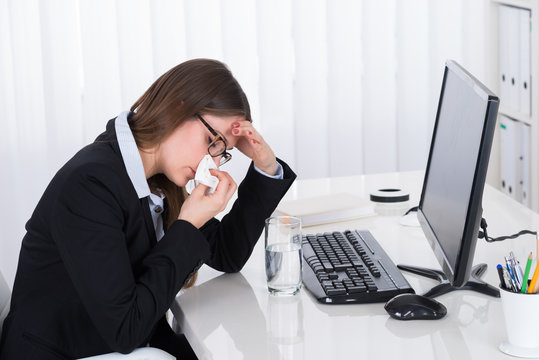 Businesswoman Blowing Her Nose At Desk