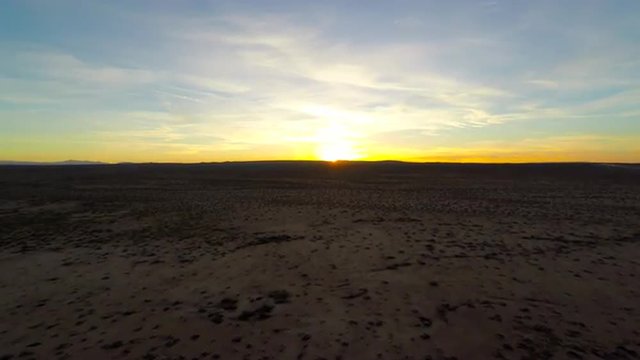 Mojave sand desert with small shrubbery but barren landscape yellow coloring sunset as 4k aerial stabilized birds eye view flying GoPro Hero4 camera booms up in the California desert 