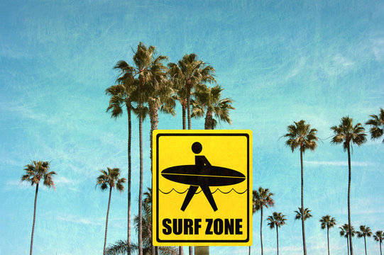 aged and worn vintage photo of surf zone sign on beach with palm trees