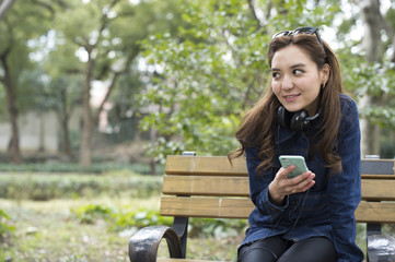 Young women are looking at the mobile phone sitting on a bench in the park