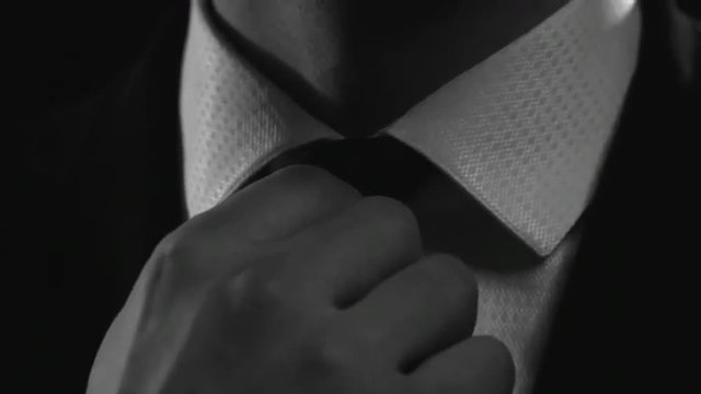 Tilt up of businessman in elegant suit and fixing his tie knot