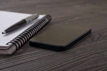 black smartphone on office workplace with notebook and pen