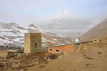 Small village in the Caucasian mountains in the winter. A cowshed, an ancient guard tower, and a modern radio tower around. North Ossetia - Alania, Russia. - 103818330