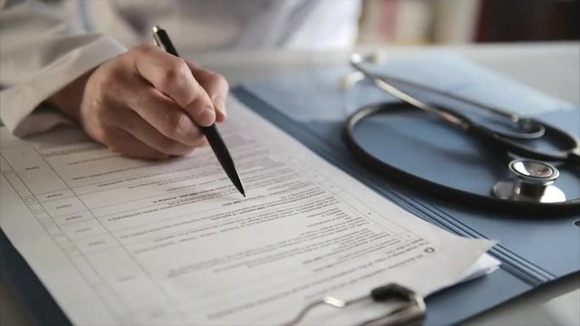 Woman physician checking medical form and drinking coffee at the table. Concept of medical tests, diagnoses and medicine prescription.  