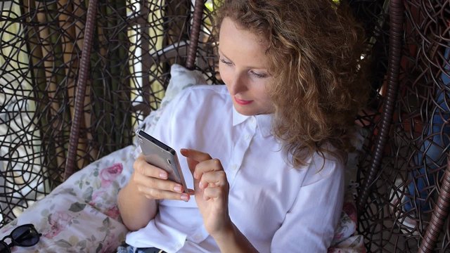Smiling Fashion Hipster Girl Uses Smart Phone in Trendy Cafe