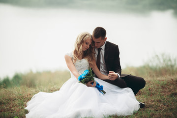 Happy wedding couple sitting on the ground near the lake