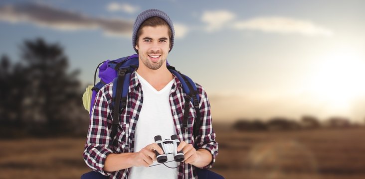 Composite image of happy hipster wearing backpack holding binoculars