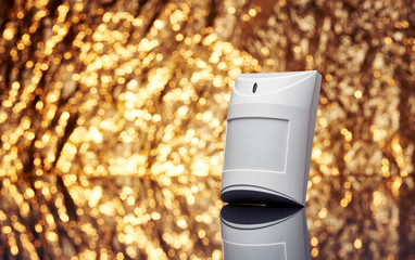 White plastic alarm motion sensor with fancy shiny gold background full of sparks out of focus.
