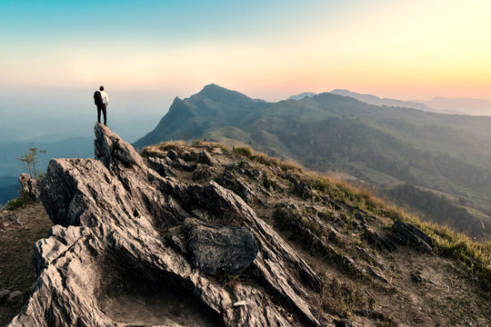 businessman hike on the peak of rocks mountain at sunset, succes