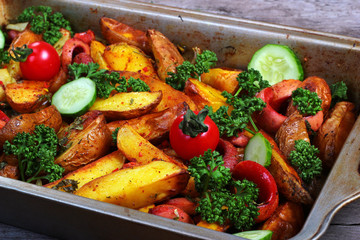 Fried potatoes with sausages, green parsley, fresh tomatos and cucumbers. Greasy pan on old wooden table.