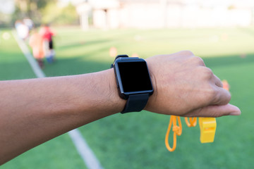 Close-up hands of Coach using his smartwatch is coaching Children Training In Soccer Team