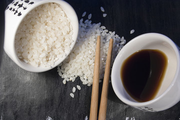 rice, soy sauce and chopsticks on a black background