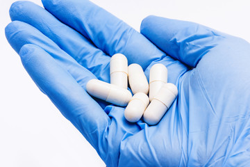 Hand in blue glove holding pills.