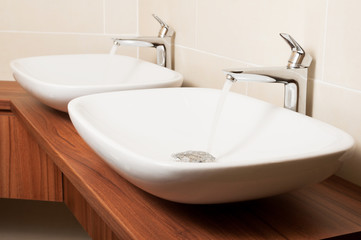 Close-up of shiny taps with flowing water and ceramic sinks