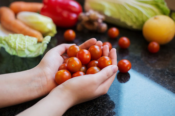 Woman holding cherry tomatoes in hands home with vegetables in background.Clouse up Cherry tomatoes in woman's hands on white background